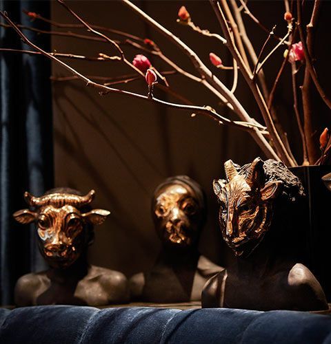 Three dark sculpted busts beneath bare branches, lit with warm dramatic light