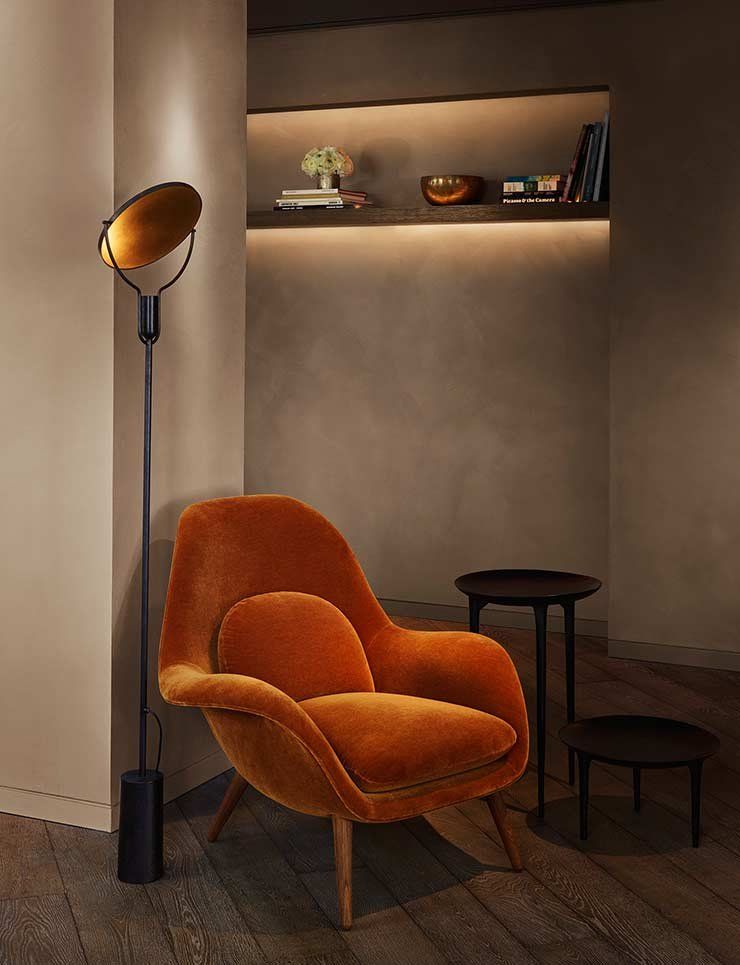 A cozy lobby area with a comfortable orange chair, a floor lamp, and a shelf with decorative items.