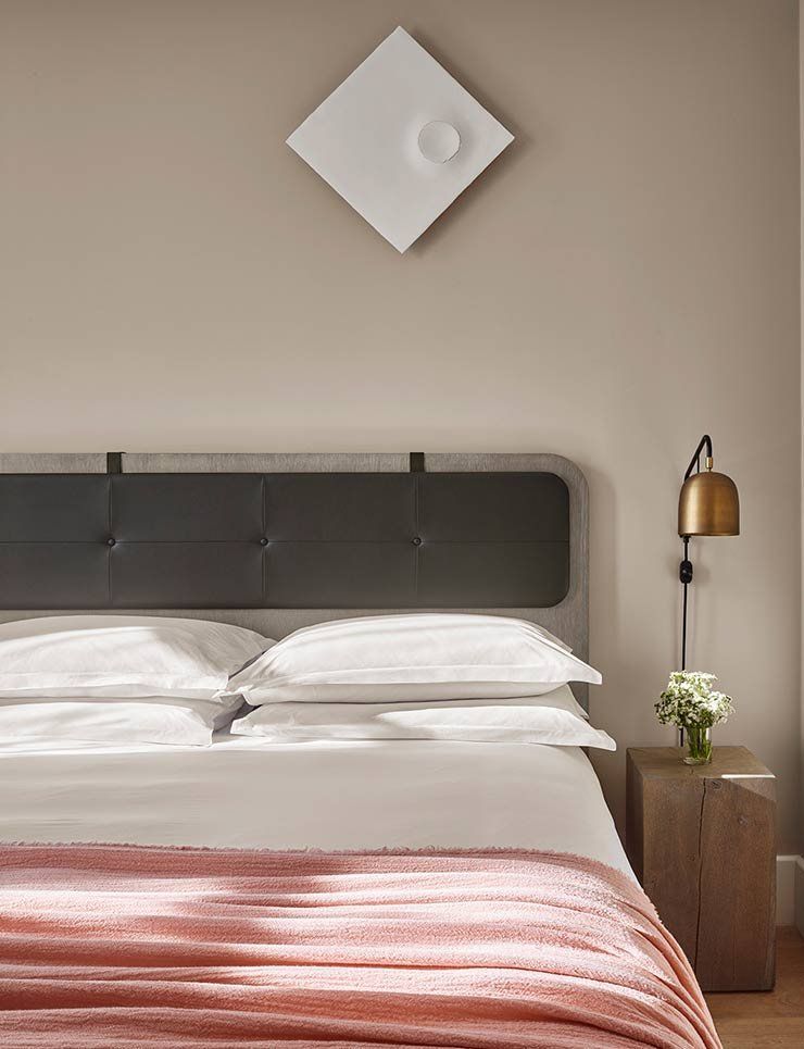 Modern bedroom with gray headboard, white bedding, pink throw, wall art, and bedside lamp