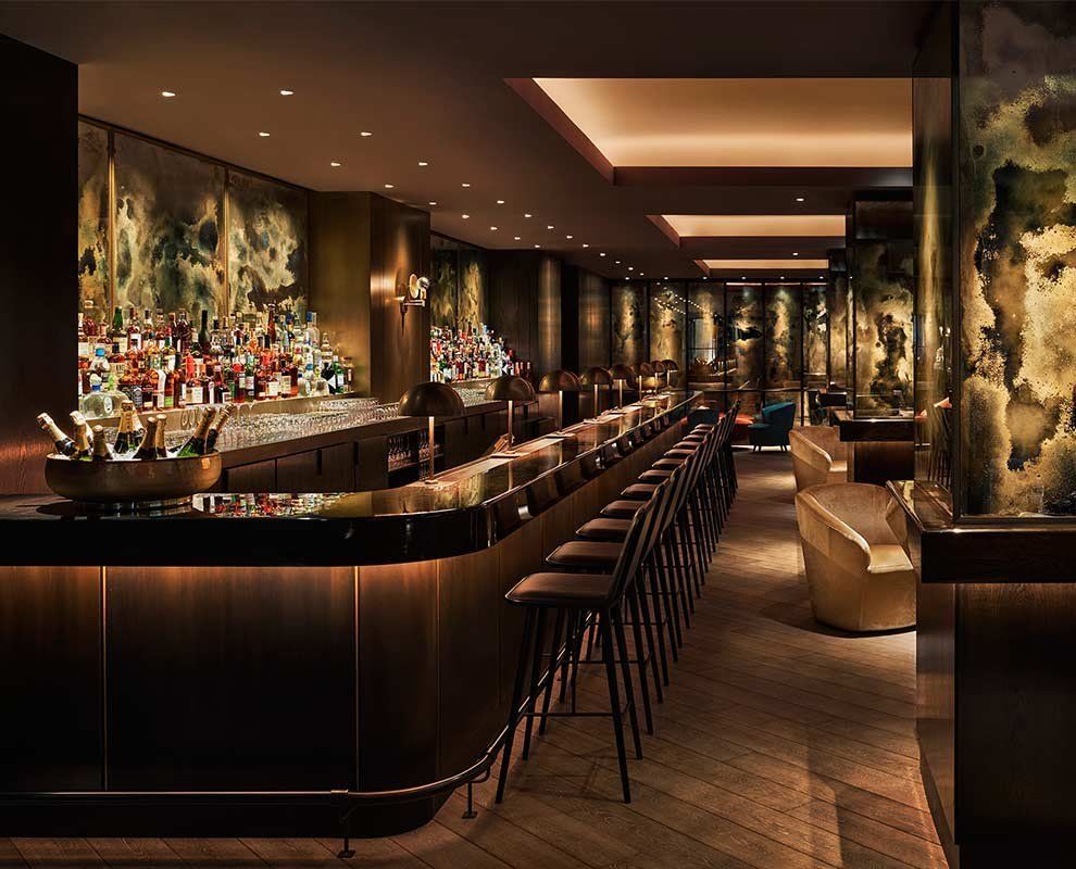 Elegant dimly lit bar with a long wooden counter, stools, and warm ambient lighting