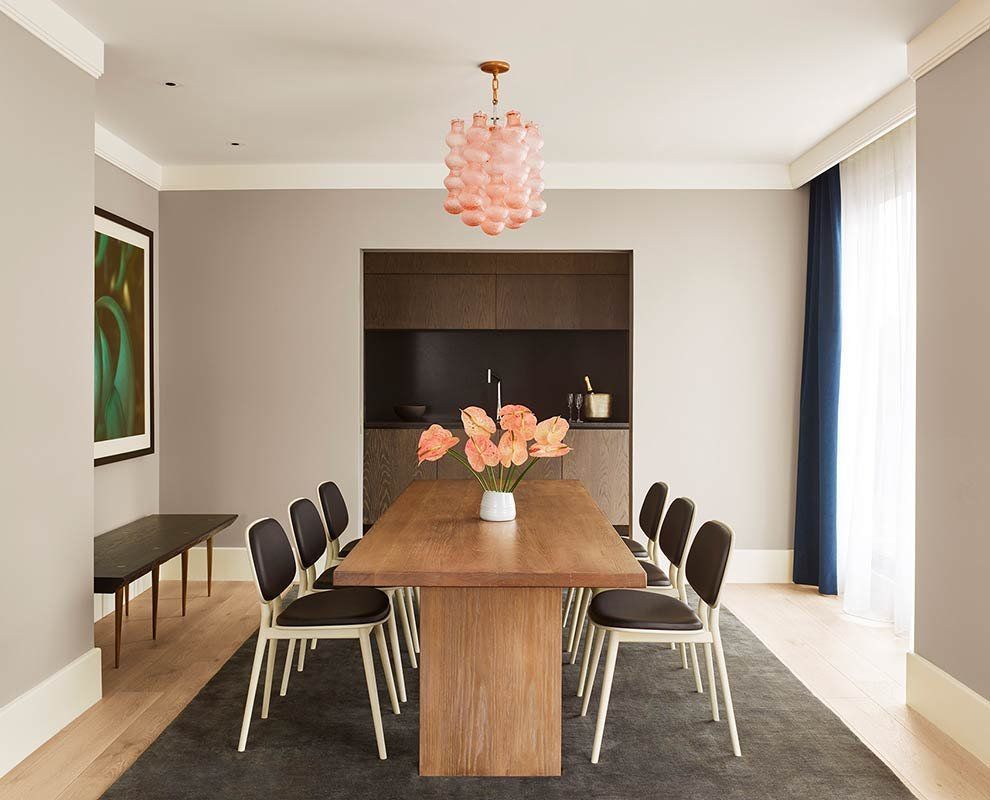Modern dining room with a wooden table, black chairs, pink chandelier, and flowers on a rug