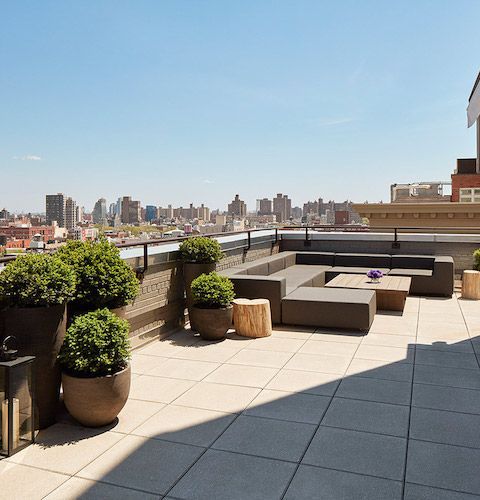 Rooftop terrace with outdoor seating, potted plants, and a city skyline under a clear blue sky