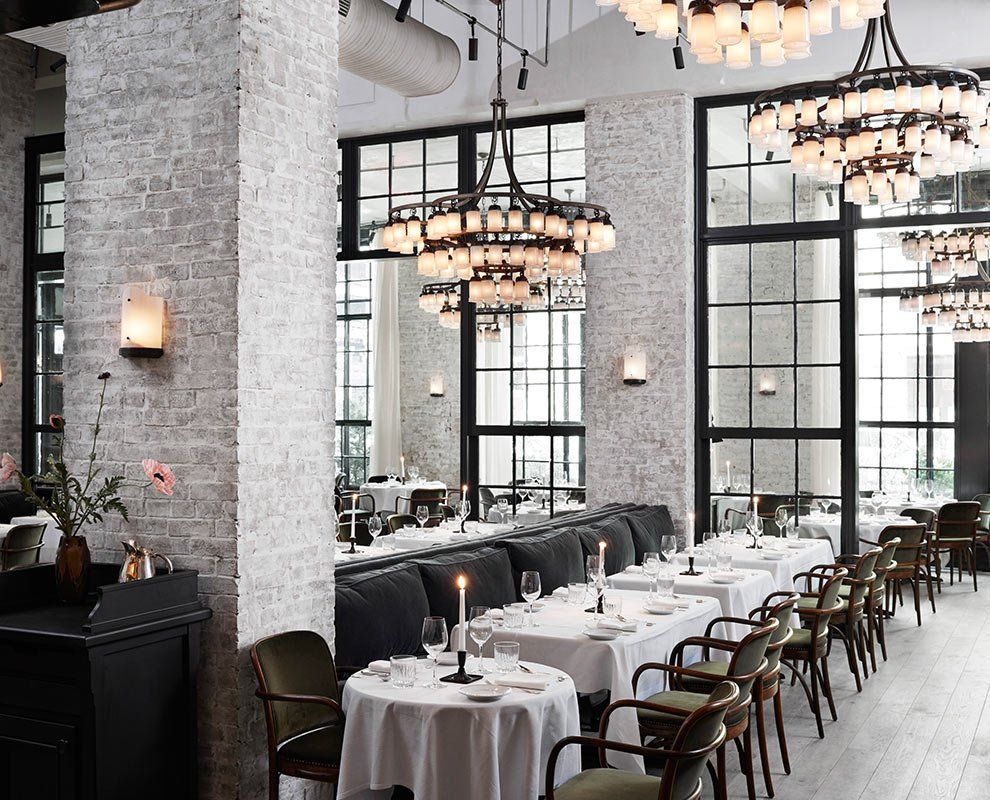 Elegant restaurant dining room with white tablecloths, black chairs, and hanging chandeliers.