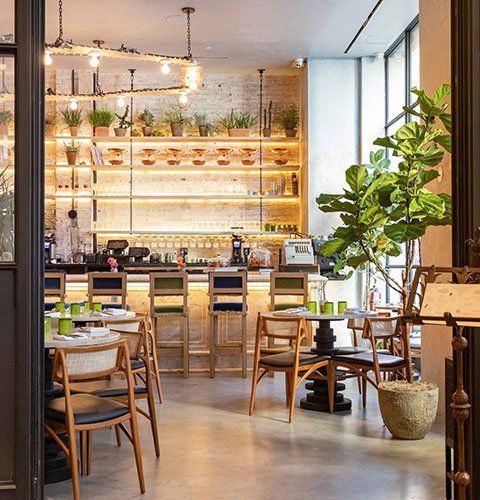 Bright modern café interior with wooden chairs, hanging lights, and a back bar lined with glasses.