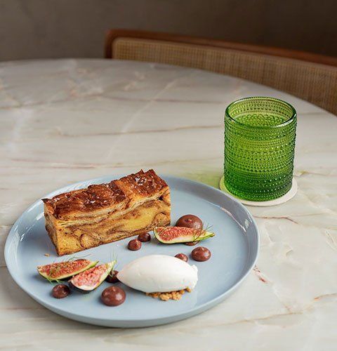 Dessert plate with cake and figs beside a green glass on a marble table