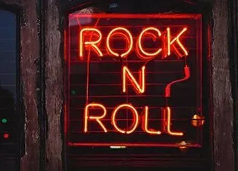 Red neon “Rock N Roll” sign glowing in a dark window