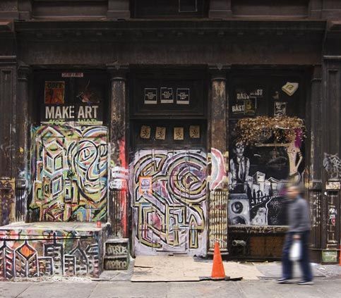 Graffiti-covered storefront with colorful murals and a blurred pedestrian passing by an orange cone.