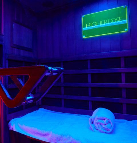 Purple neon-lit room with a bed, rolled towel, and glowing sign on the wall