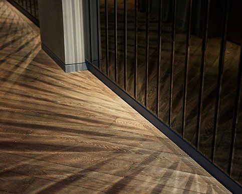 Sunlight casting striped shadows across a hardwood floor beside a black metal railing and wall corner