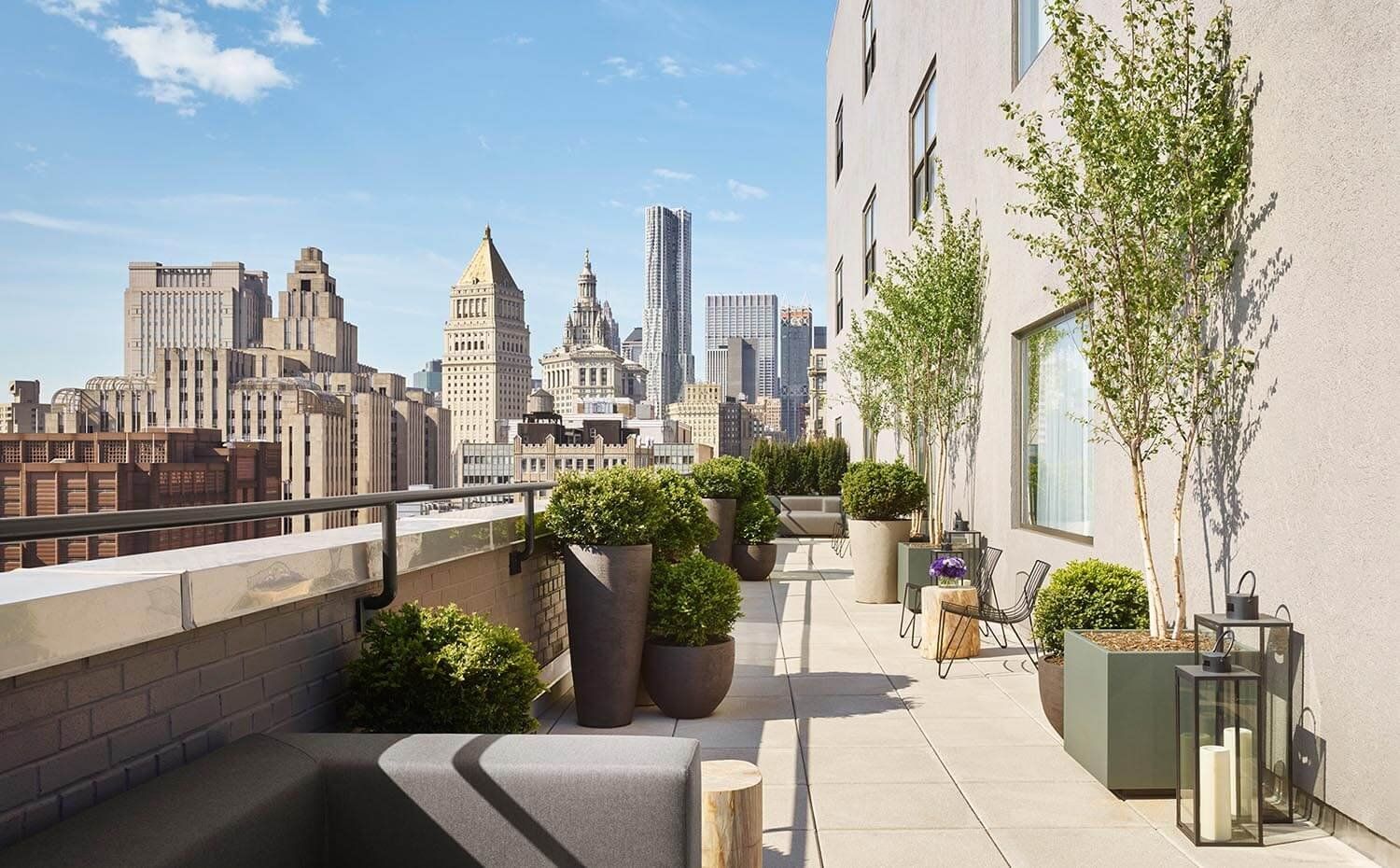 A rooftop terrace with a city skyline view, potted plants, and outdoor seating.