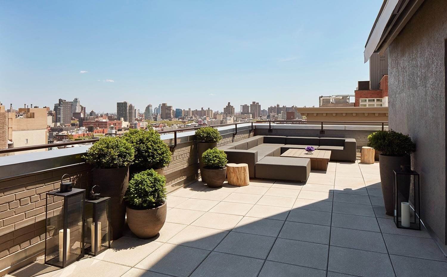 A rooftop patio with a seating area, potted plants, and a city skyline view.
