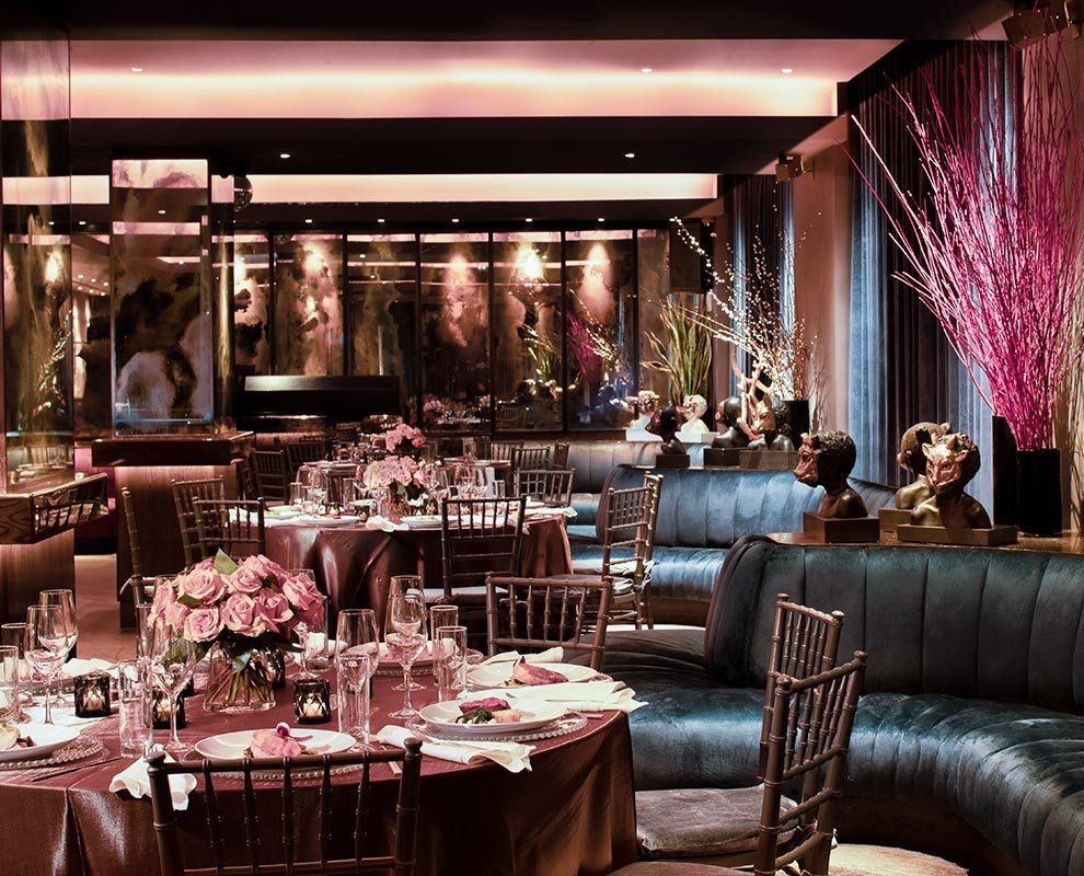 Elegant dimly lit restaurant with pink floral centerpieces, teal banquettes, and mirrored walls