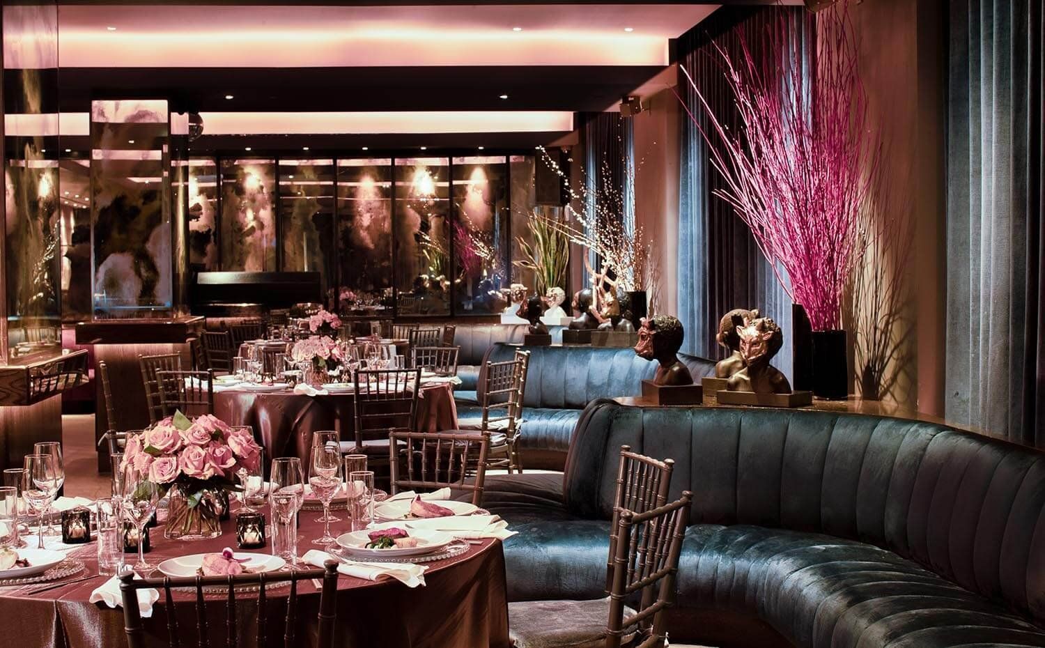 A dining area with tables set for a meal, flowers, and a couch.