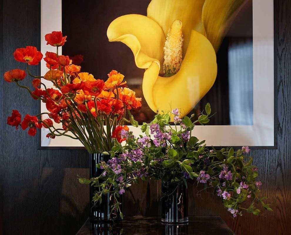 Vibrant floral arrangement with orange, purple, and yellow flowers in front of a large yellow flower painting
