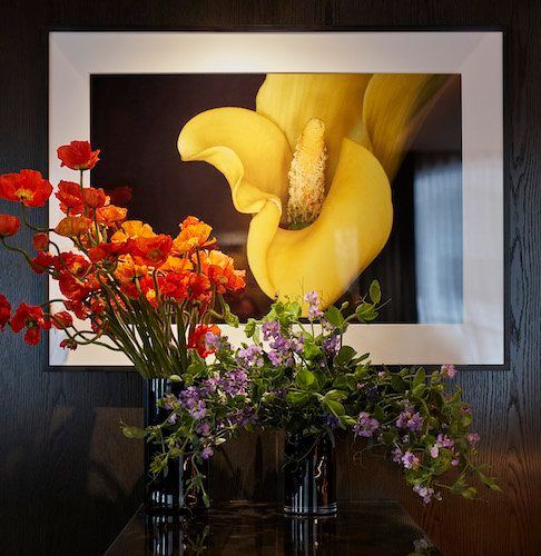 Yellow calla lily artwork with red and purple flowers arranged in vases on a dark table