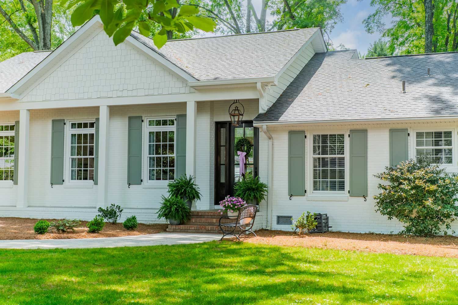 A white house with gray shutters is sitting on top of a lush green lawn.