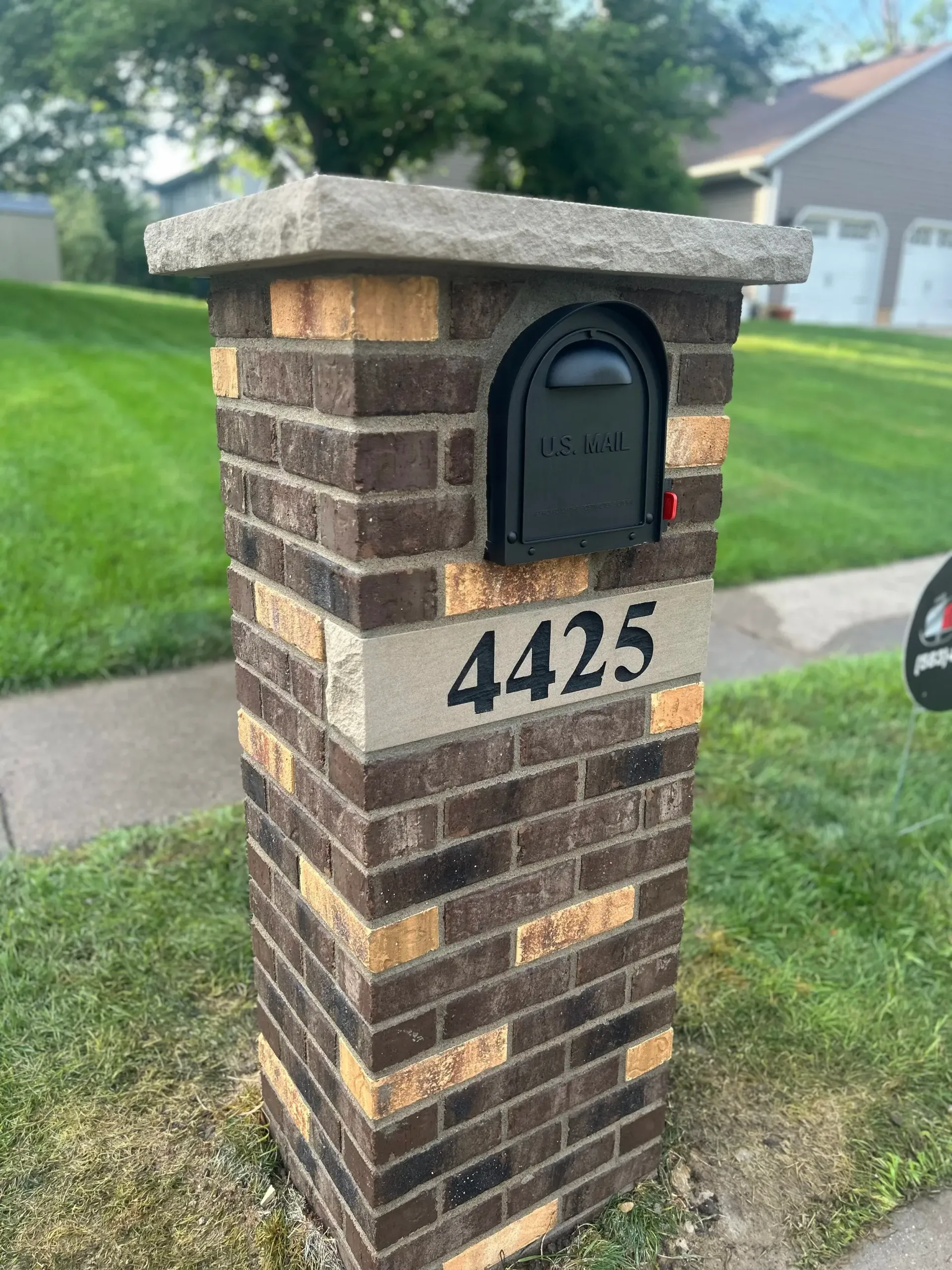 Brick mailbox pillar with black mailbox and house number 4425 beside a grassy lawn