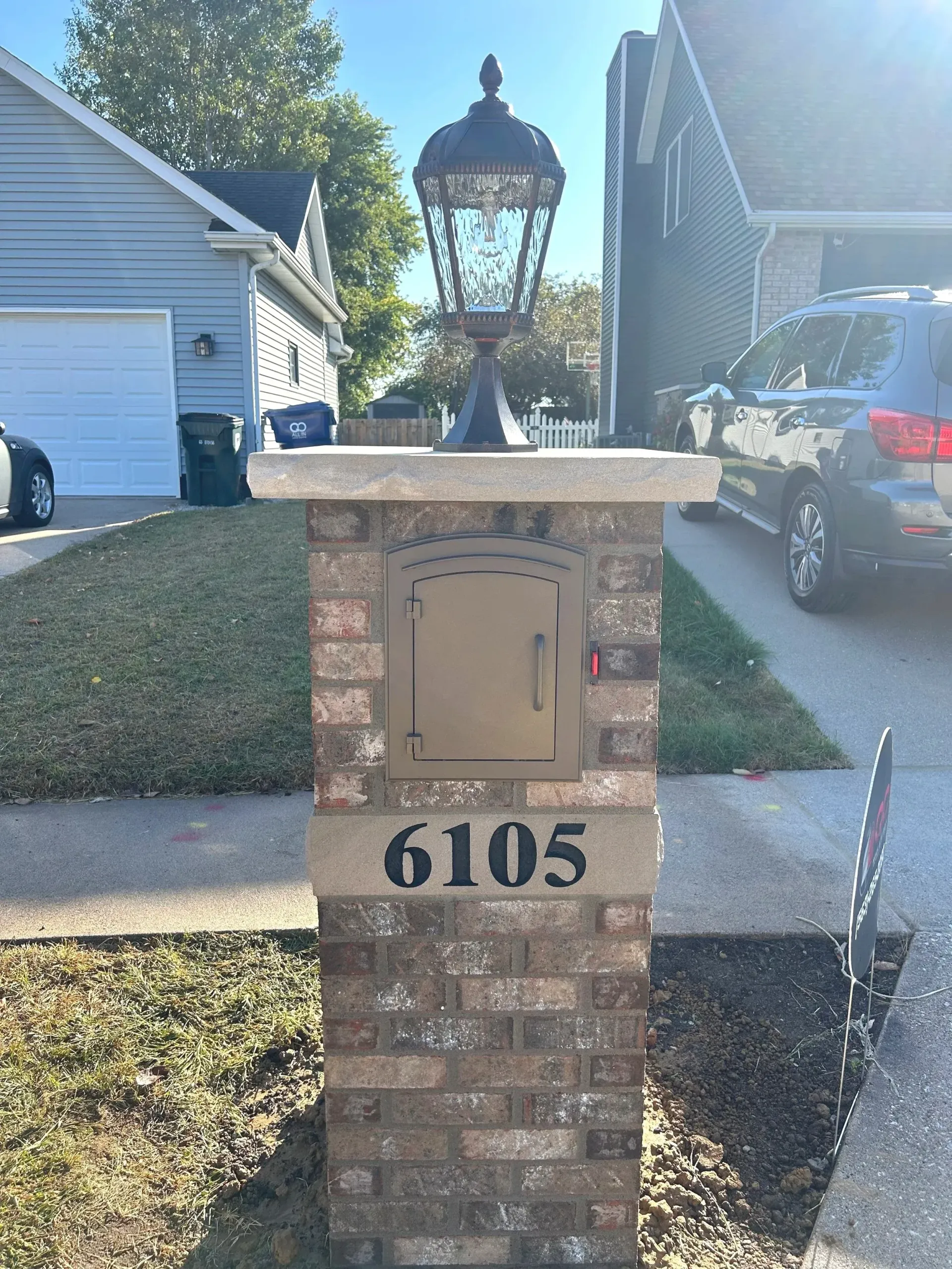 Brick mailbox pillar with lantern and house number 6105 in a suburban driveway.