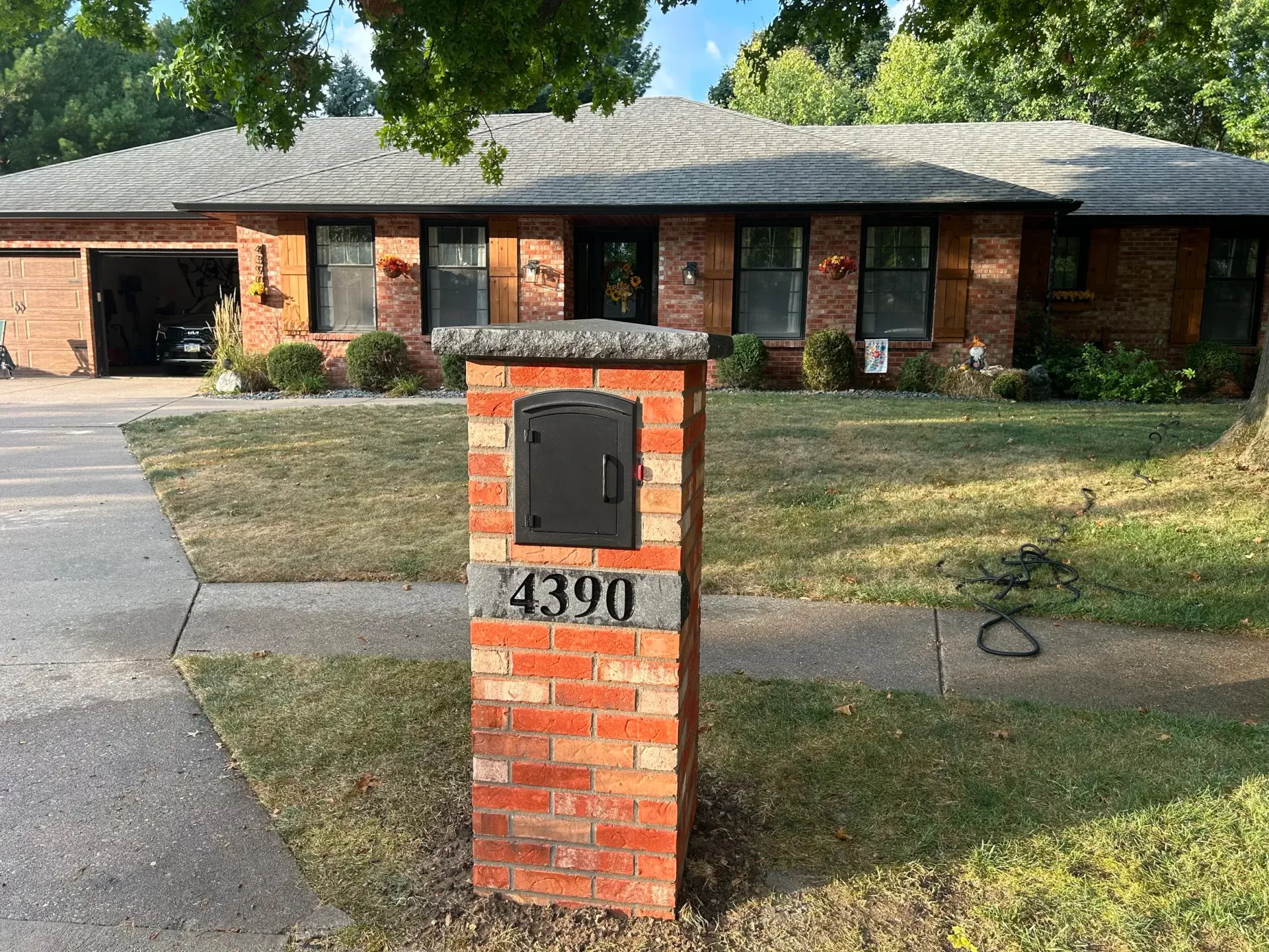Brick mailbox with house number 390 in front of a single-story brick home and driveway