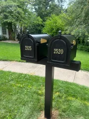 Black double mailbox with house numbers 2525 and 2520 on a lawn beside a house and trees