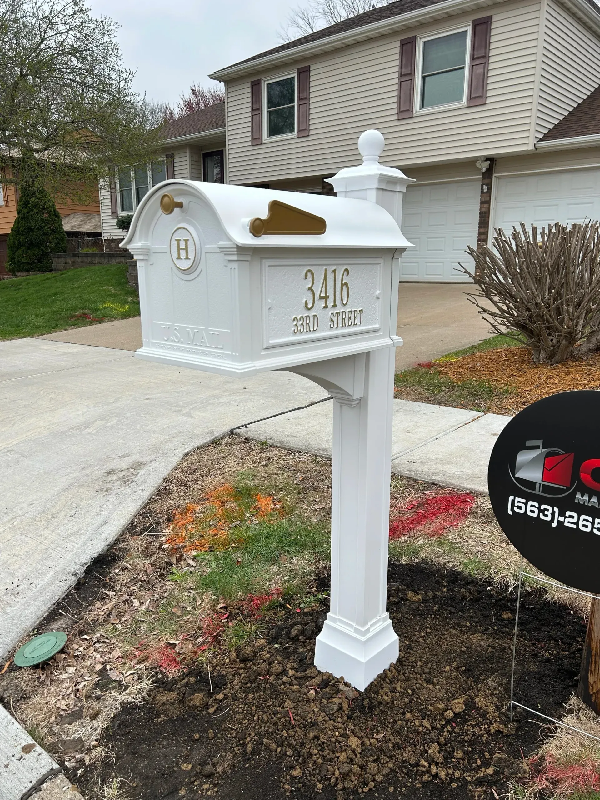 White mailbox with gold house numbers in front of a suburban home and driveway