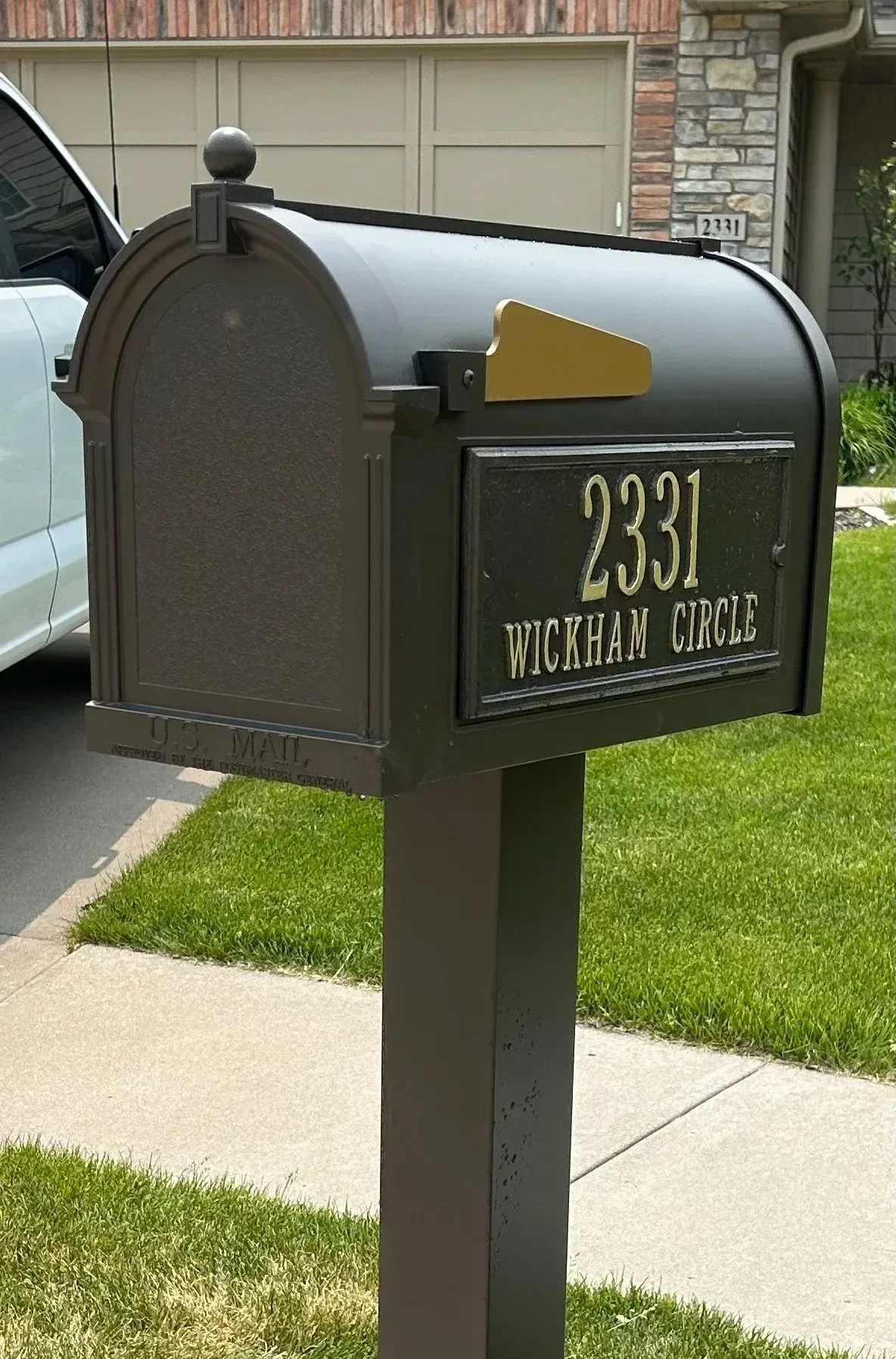 Black mailbox with gold flag and house number 2331 on a suburban sidewalk lawn.