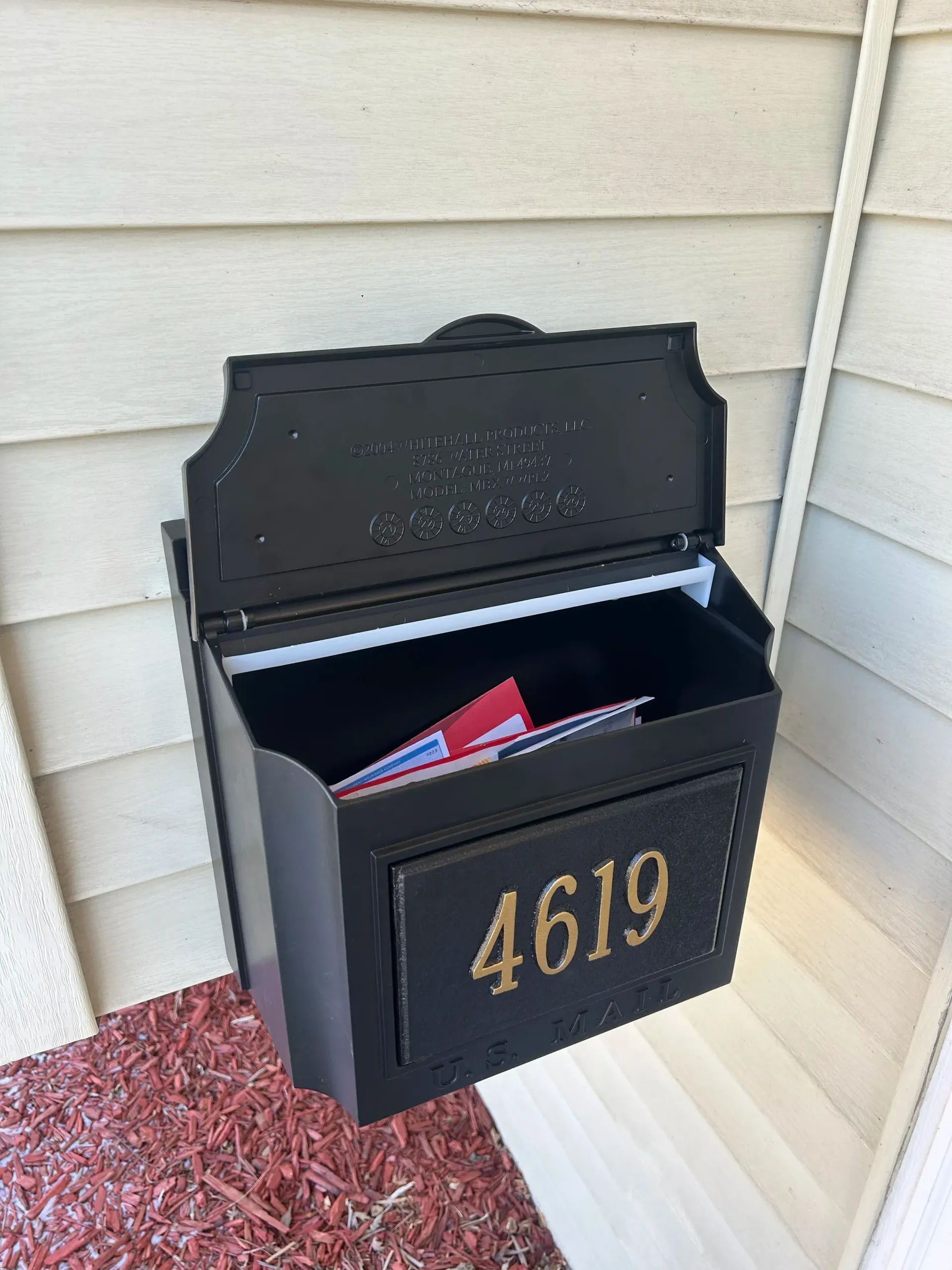 Black wall-mounted mailbox with house number 4619 open on a porch