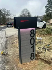 Black mailbox on post with vertical house number 8018 beside white truck on gravel driveway