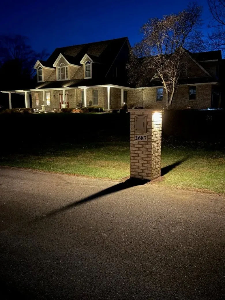 Nighttime view of a large lit house with a brick mailbox at the end of a driveway
