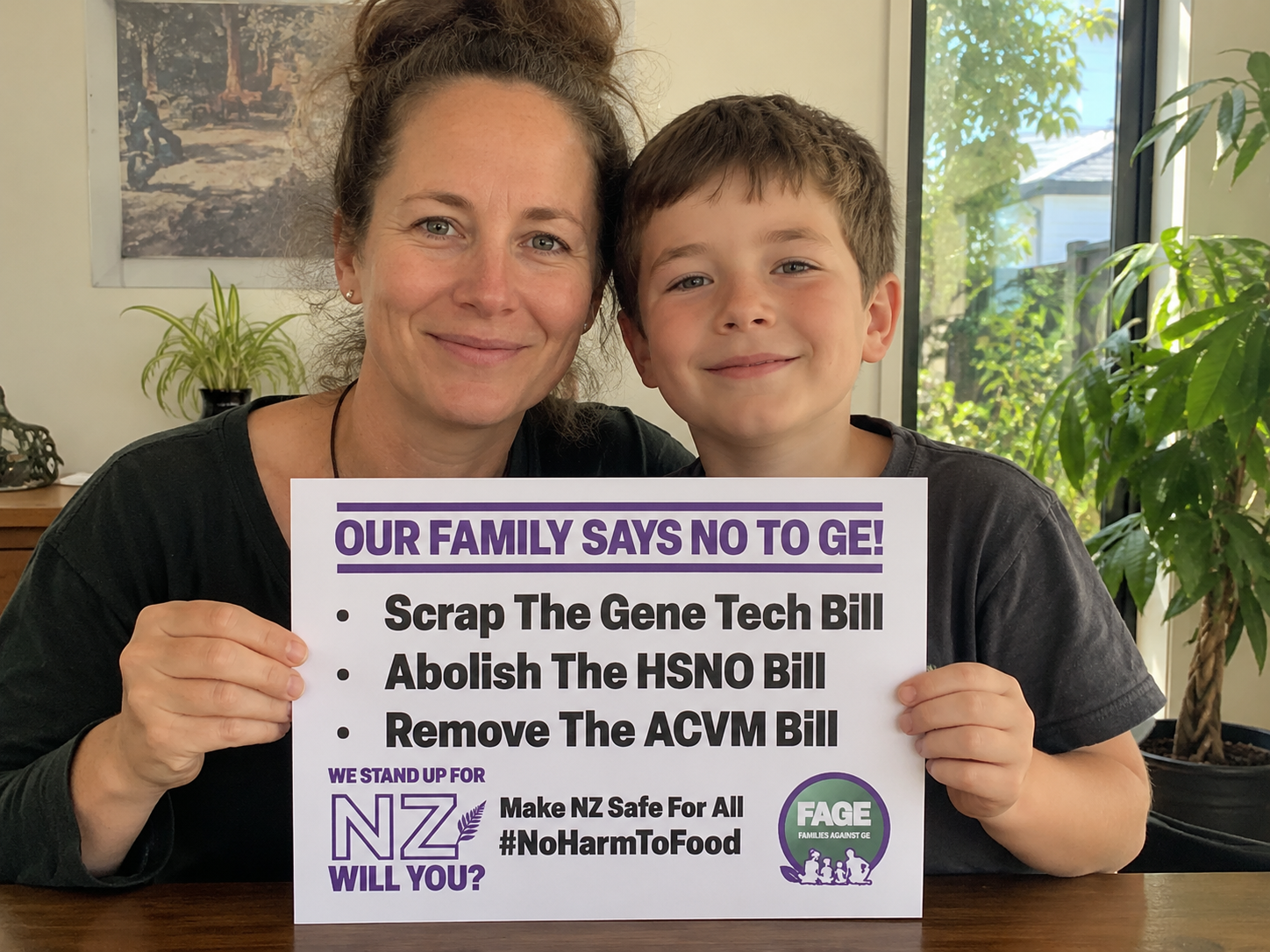 Mum and child holding a protest sign that says “Our family says no to GE. Scrap The Gene Tech Bill. Abolish The HSNO Bill” Families Against GE, NZ logo.