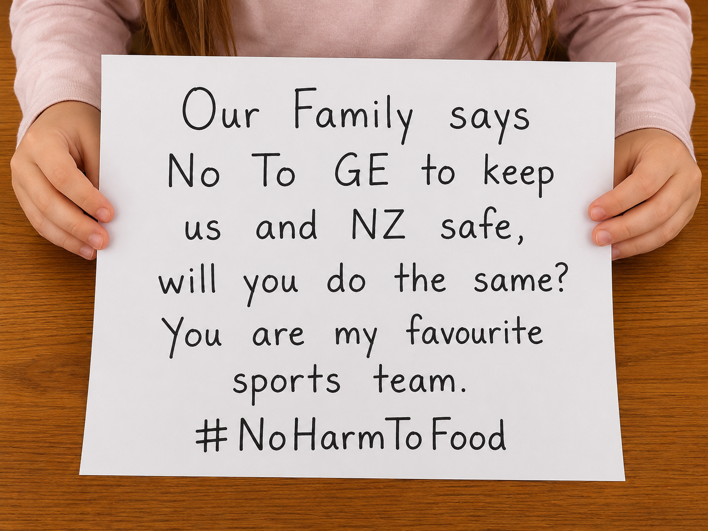 Child  holding a sign reading “Our Family says No To GE to keep us and NZ safe, will you do the same? #NoHarmToFood”