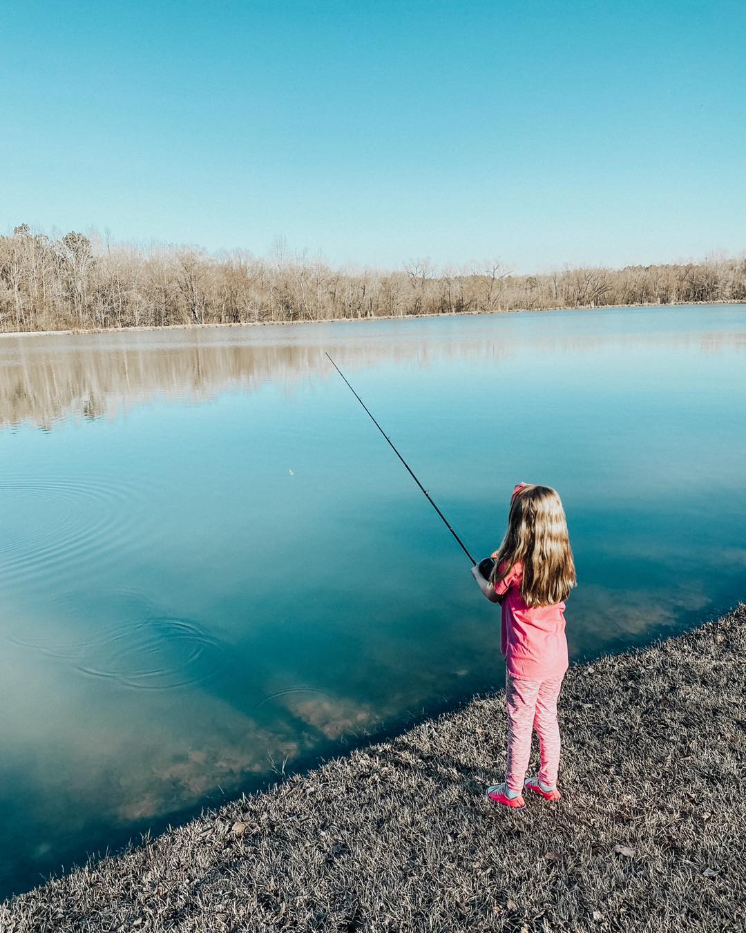 A little girl is fishing in a lake with a fishing rod.