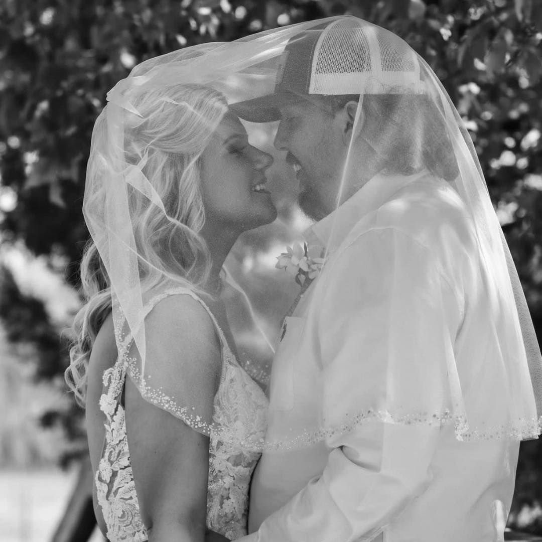 A bride and groom are kissing under a veil in a black and white photo.