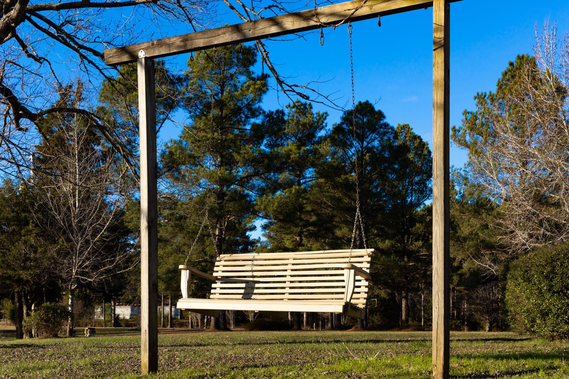 A white wooden swing is hanging from a wooden post in a park.