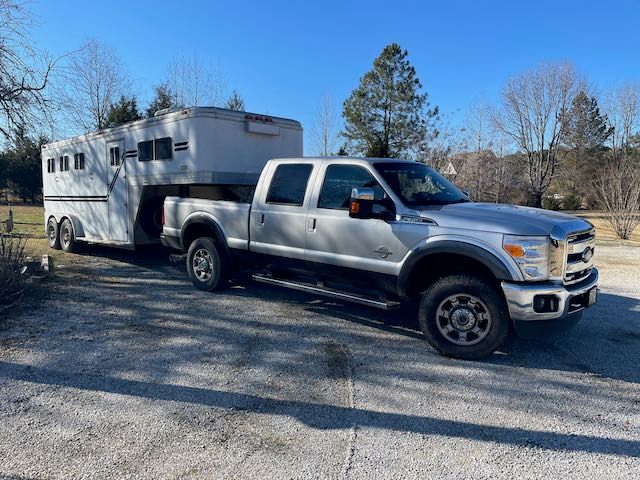 A silver truck is towing a horse trailer in a parking lot.