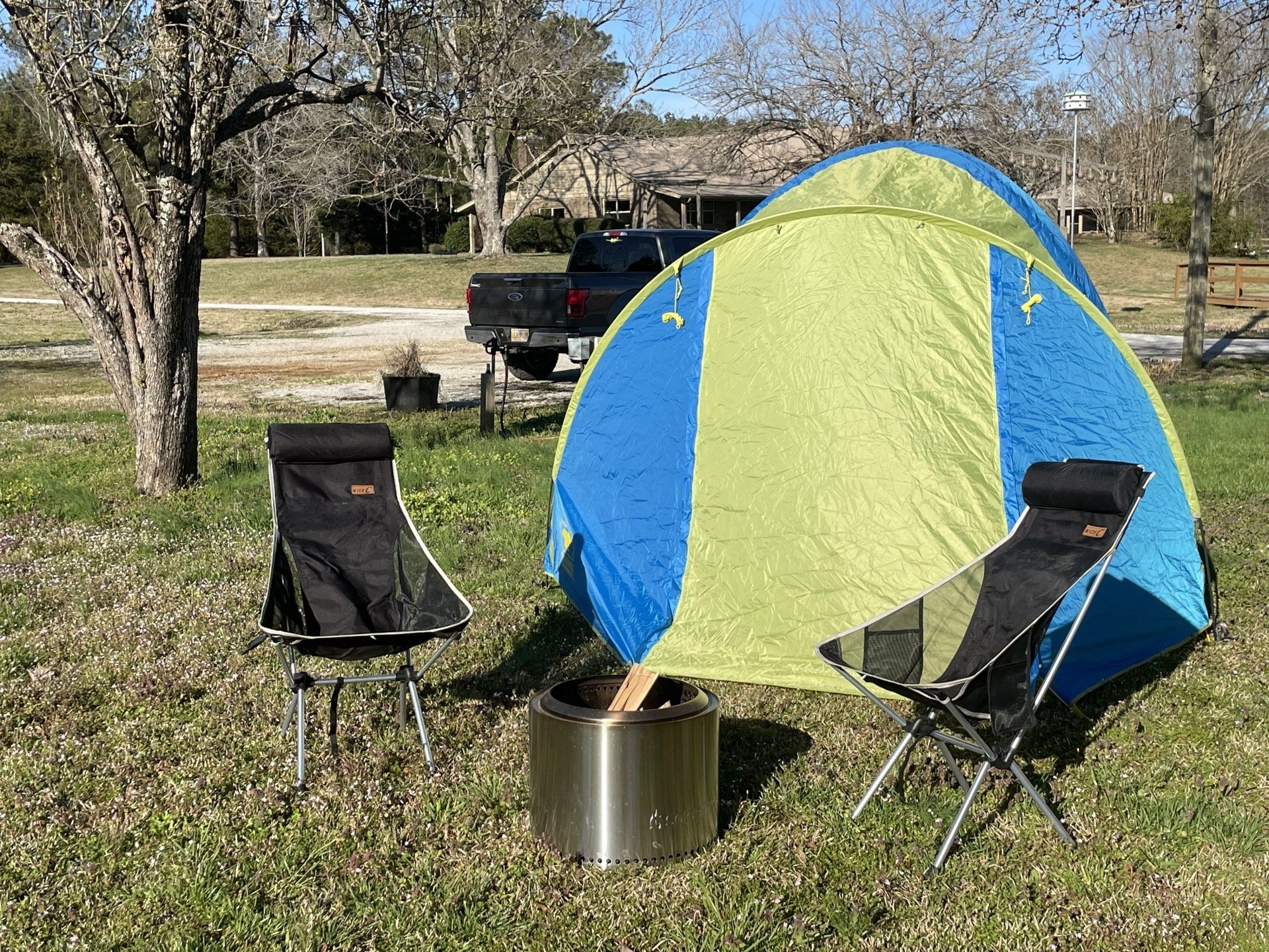 A tent and chairs are sitting next to a fire pit in a field.