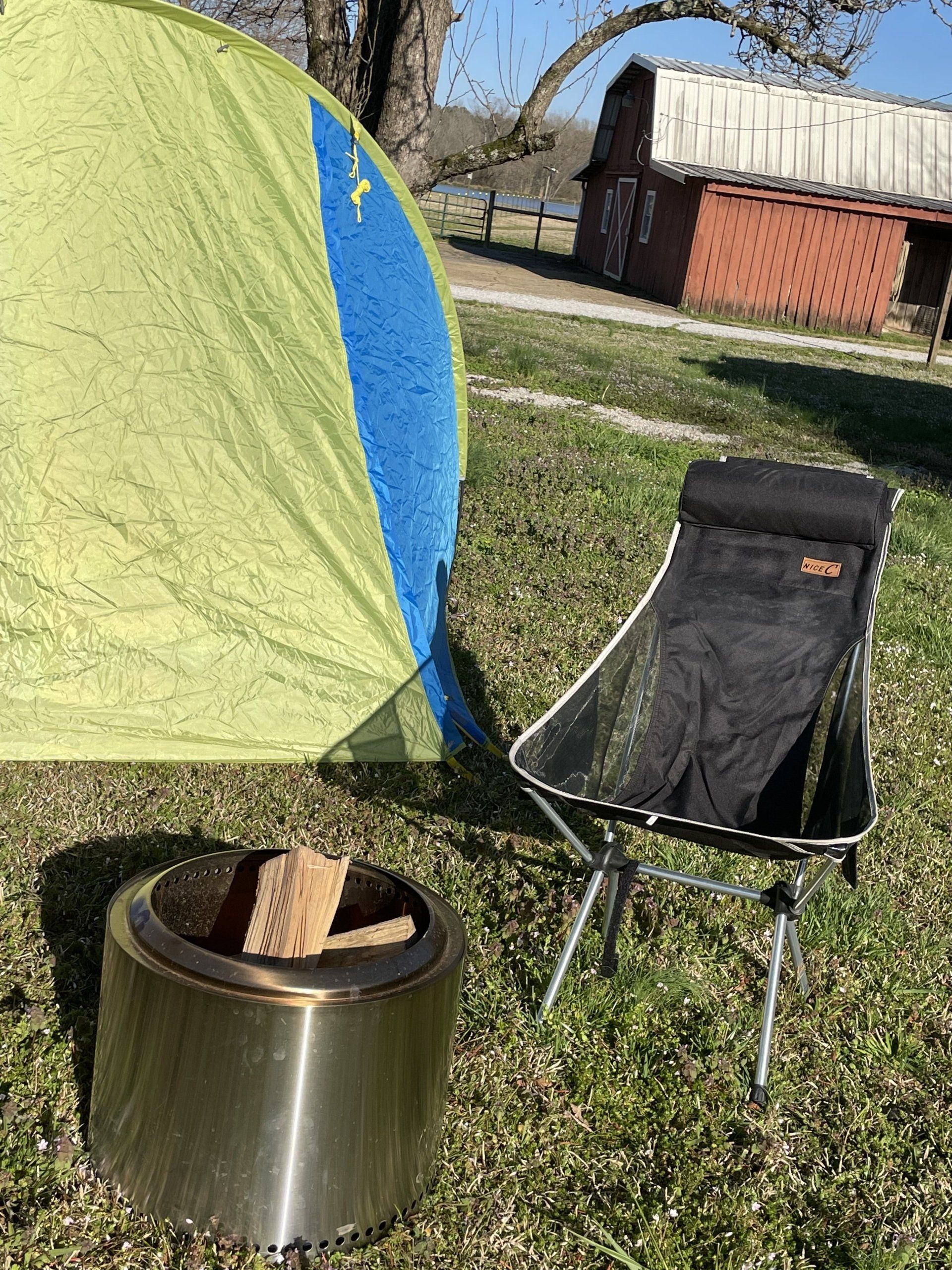 A tent and a chair are sitting next to a fire pit in the grass.