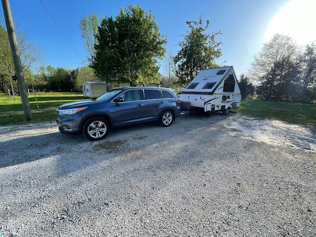 A car is towing a trailer in a gravel lot.