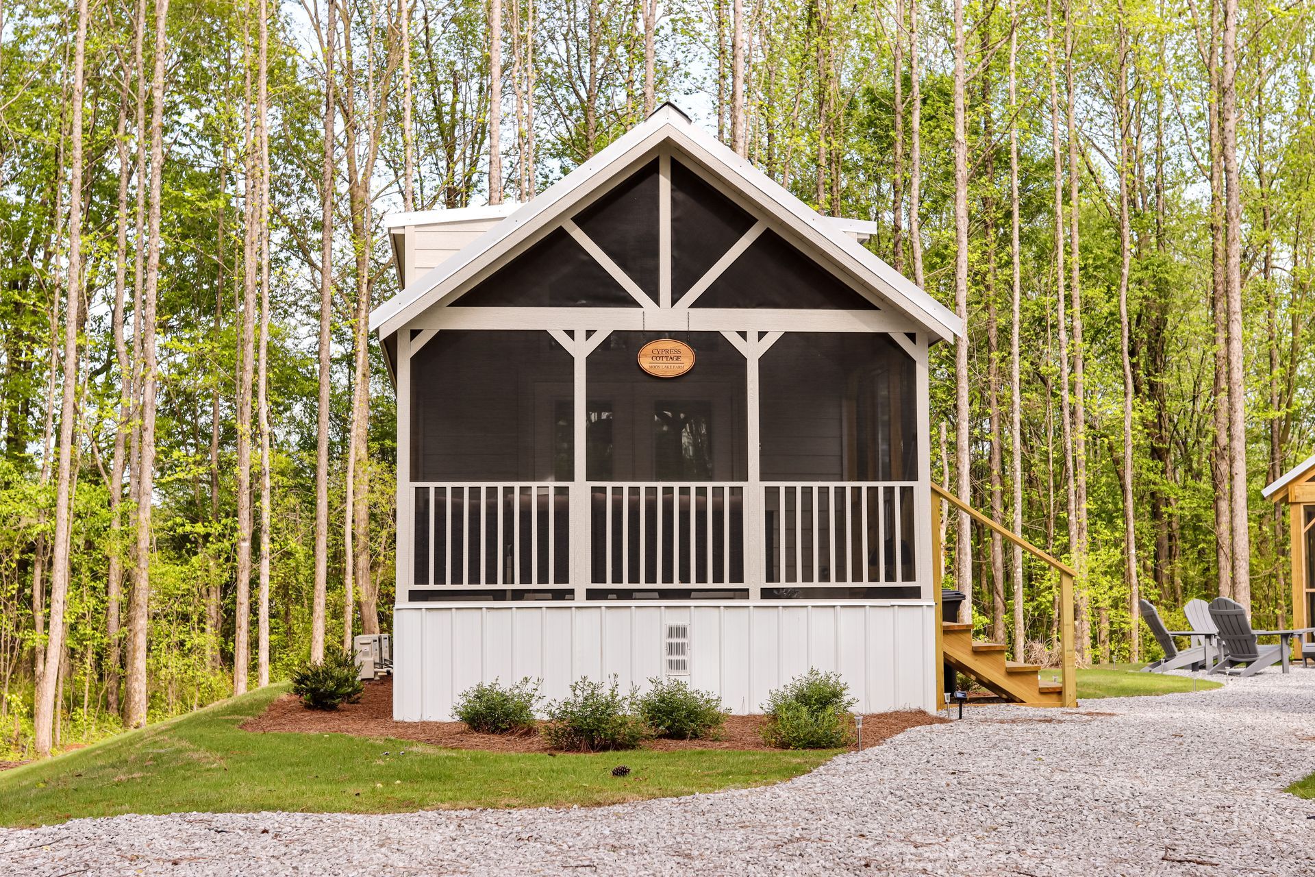 A small house with a screened in porch in the middle of a forest.