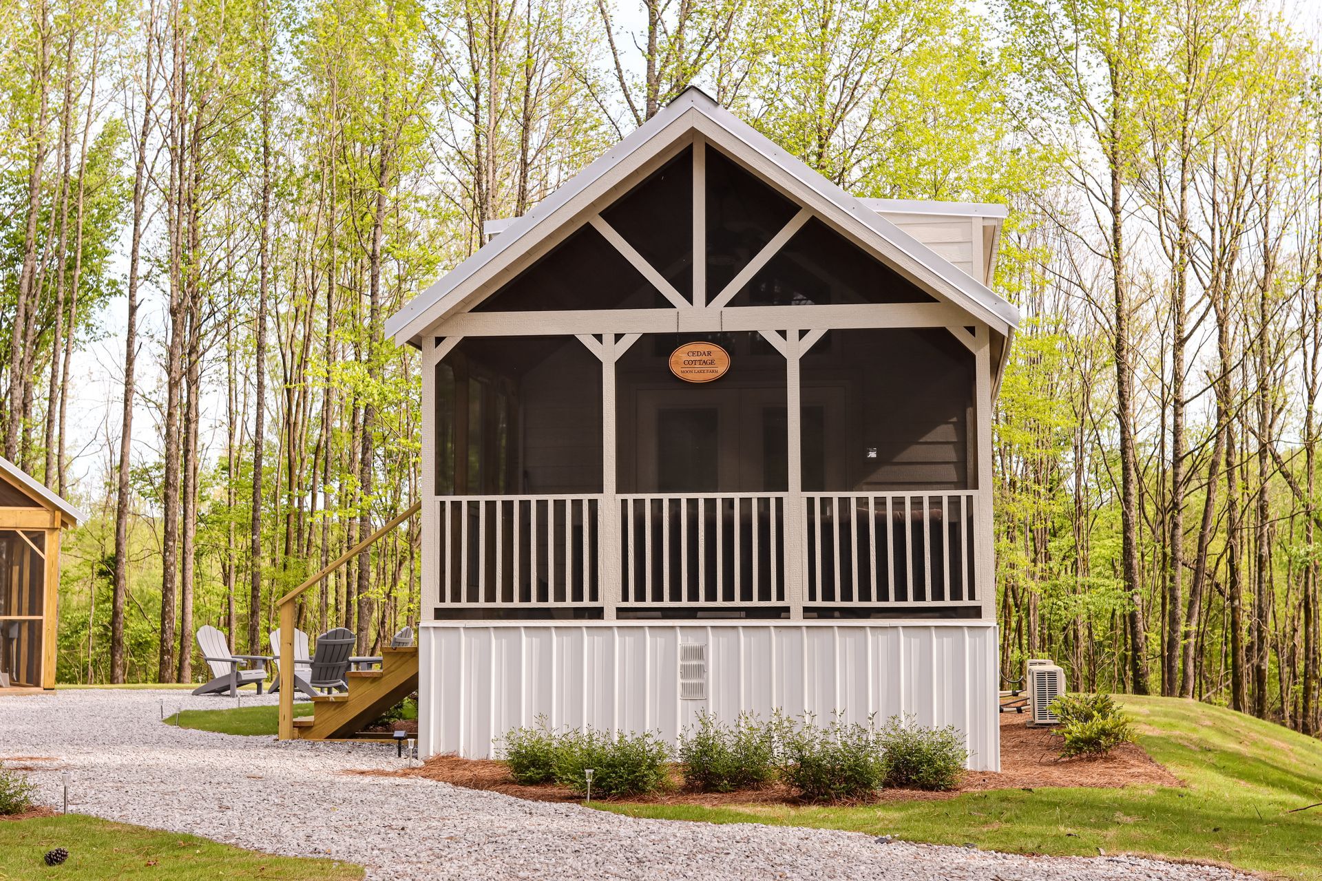 A small white house with a screened in porch in the woods.