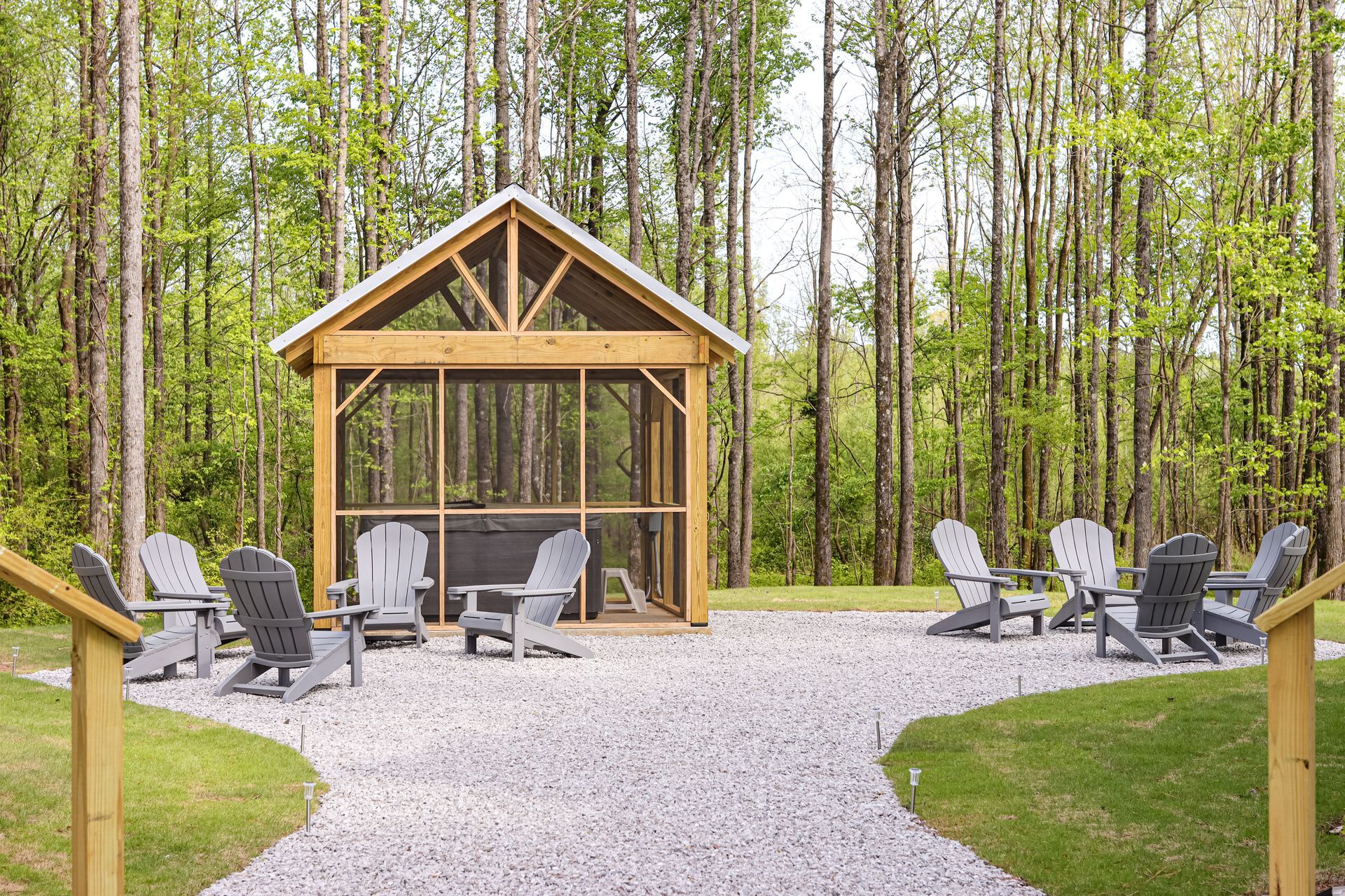 A gazebo in the middle of a forest with chairs around it.