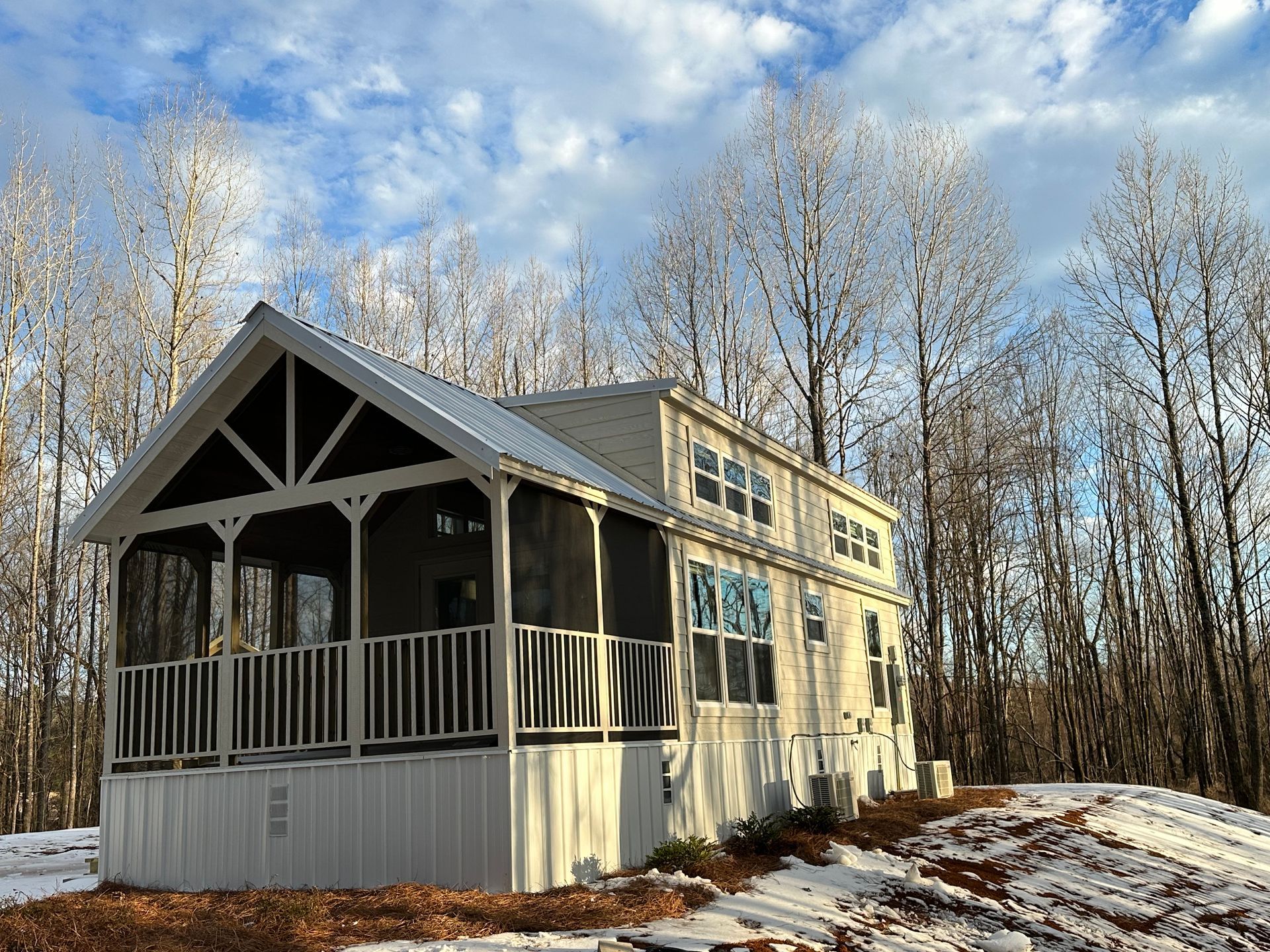 A white house with a screened in porch in the woods