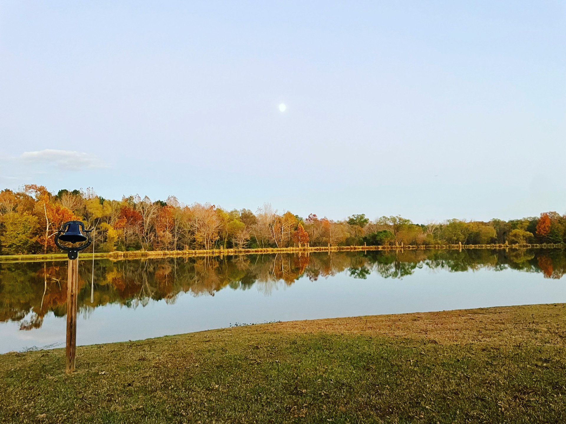 A lake with trees in the background and a full moon in the sky.