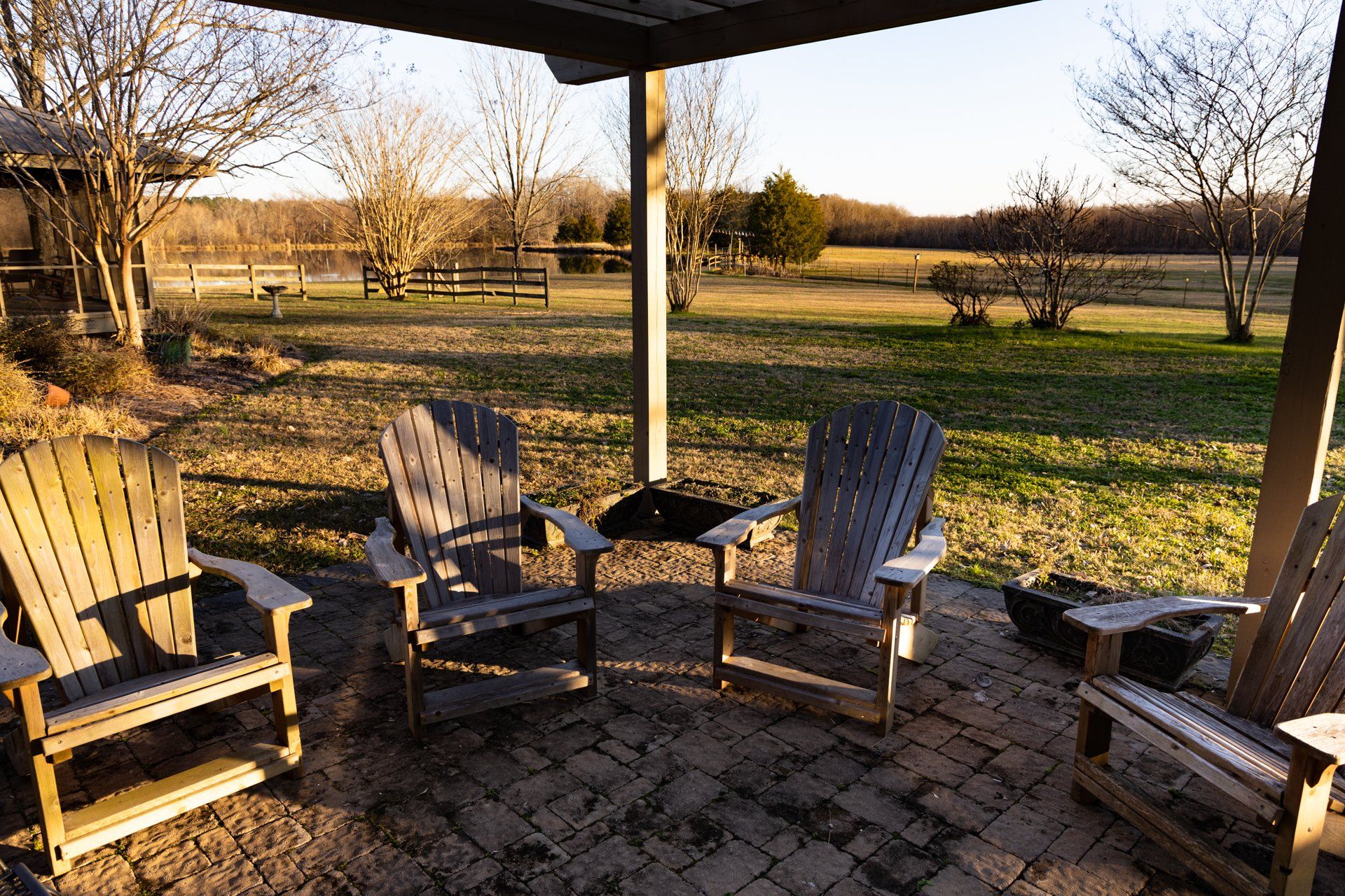 A group of wooden chairs are sitting under a pergola on a patio.