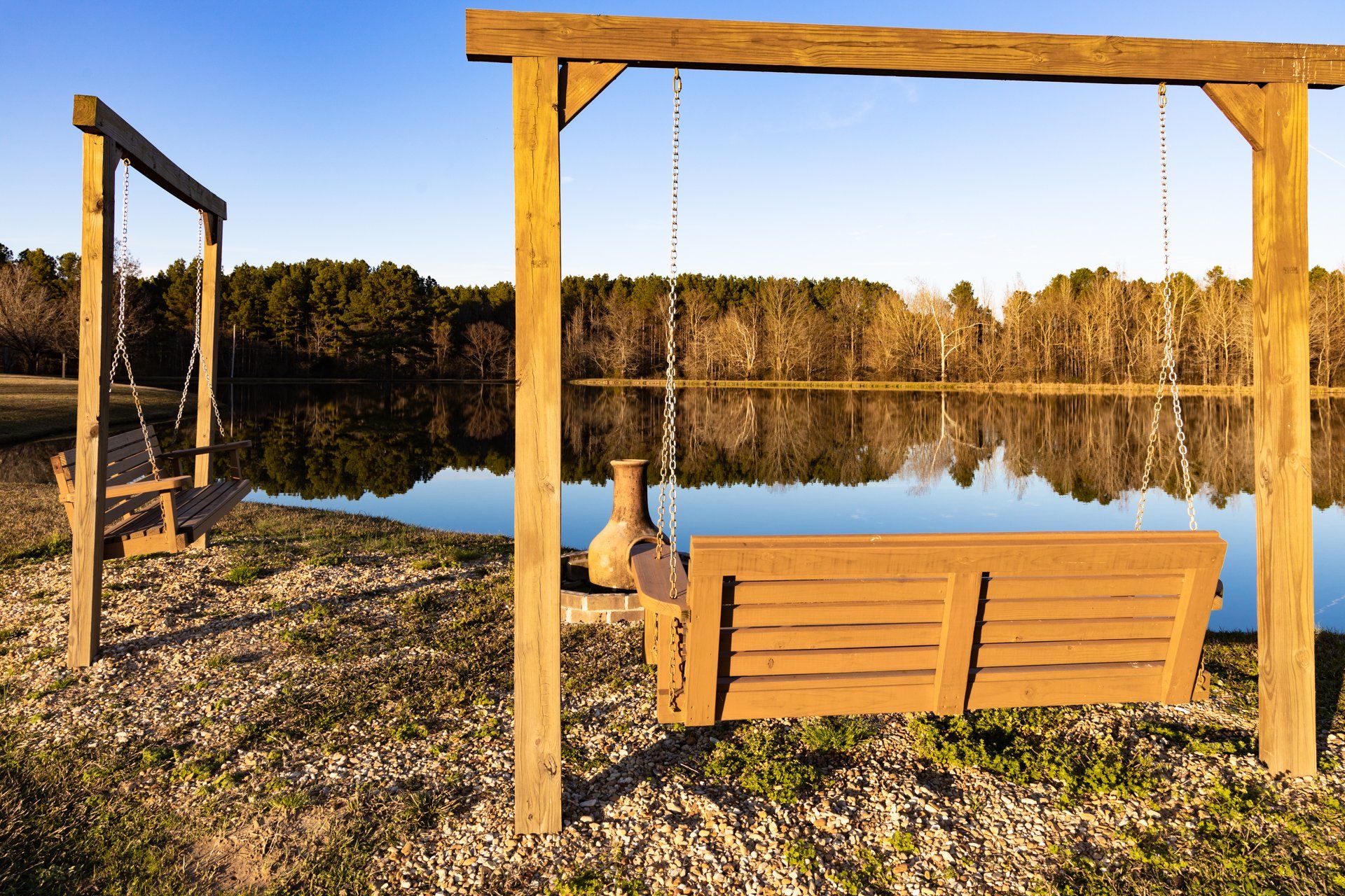 Two wooden swings are sitting next to a lake.