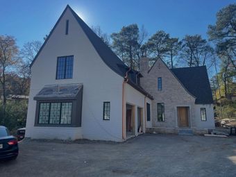 Old house under renovation with stone chimney, construction materials, and trees surrounding it