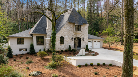 Stone house in a wooded yard, with landscaping work and a Red Contract sign in the foreground