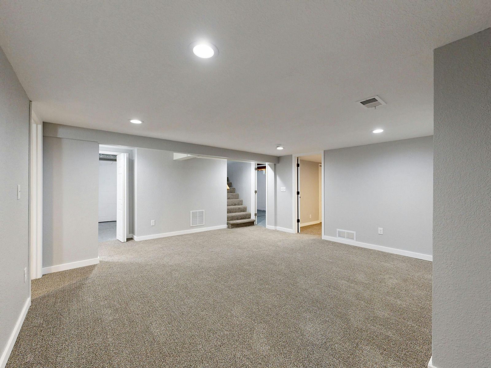 Carpeted staircase beside a bright upstairs hallway and open room with balcony doors
