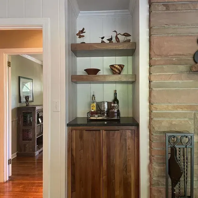 Built-in wall shelf with decor and bottles beside a stone fireplace in a home hallway