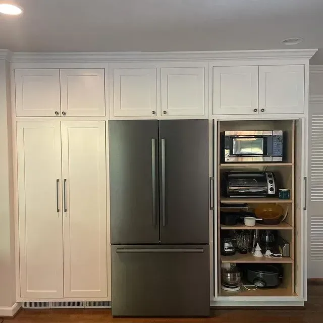 White kitchen cabinetry with a stainless steel fridge and an open pantry holding appliances and dishes